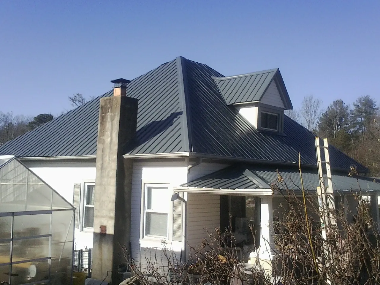 Dark blue standing seam metal roof on a white farmhouse with dormer — Slate & Tile Roof Repair by Roofing Brothers in Chimayo