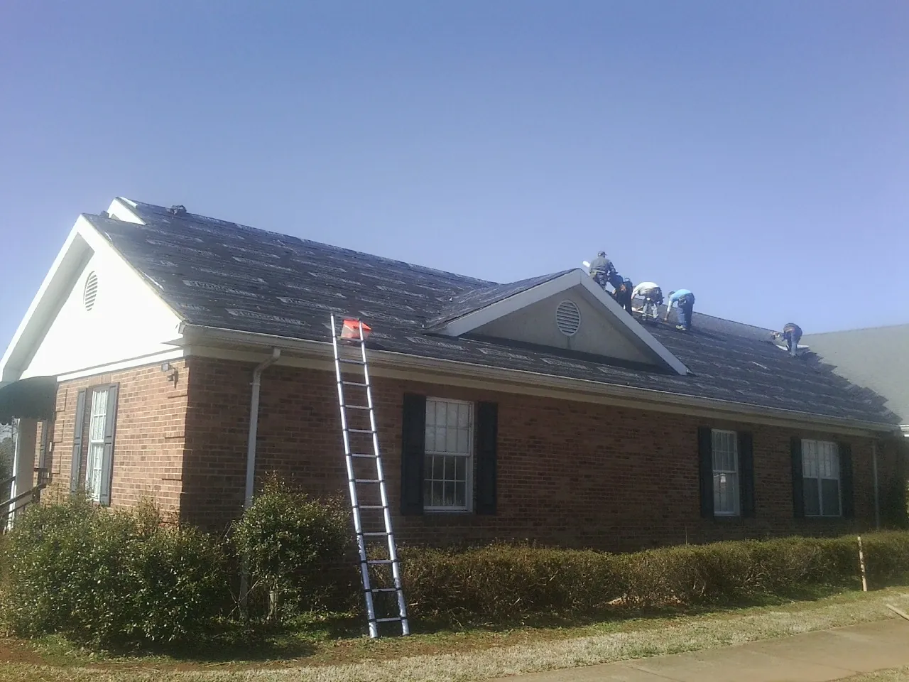 Crew tearing shingles off a brick ranch roof with a ladder set — Emergency Roof Repair work by our crew in Chimayo