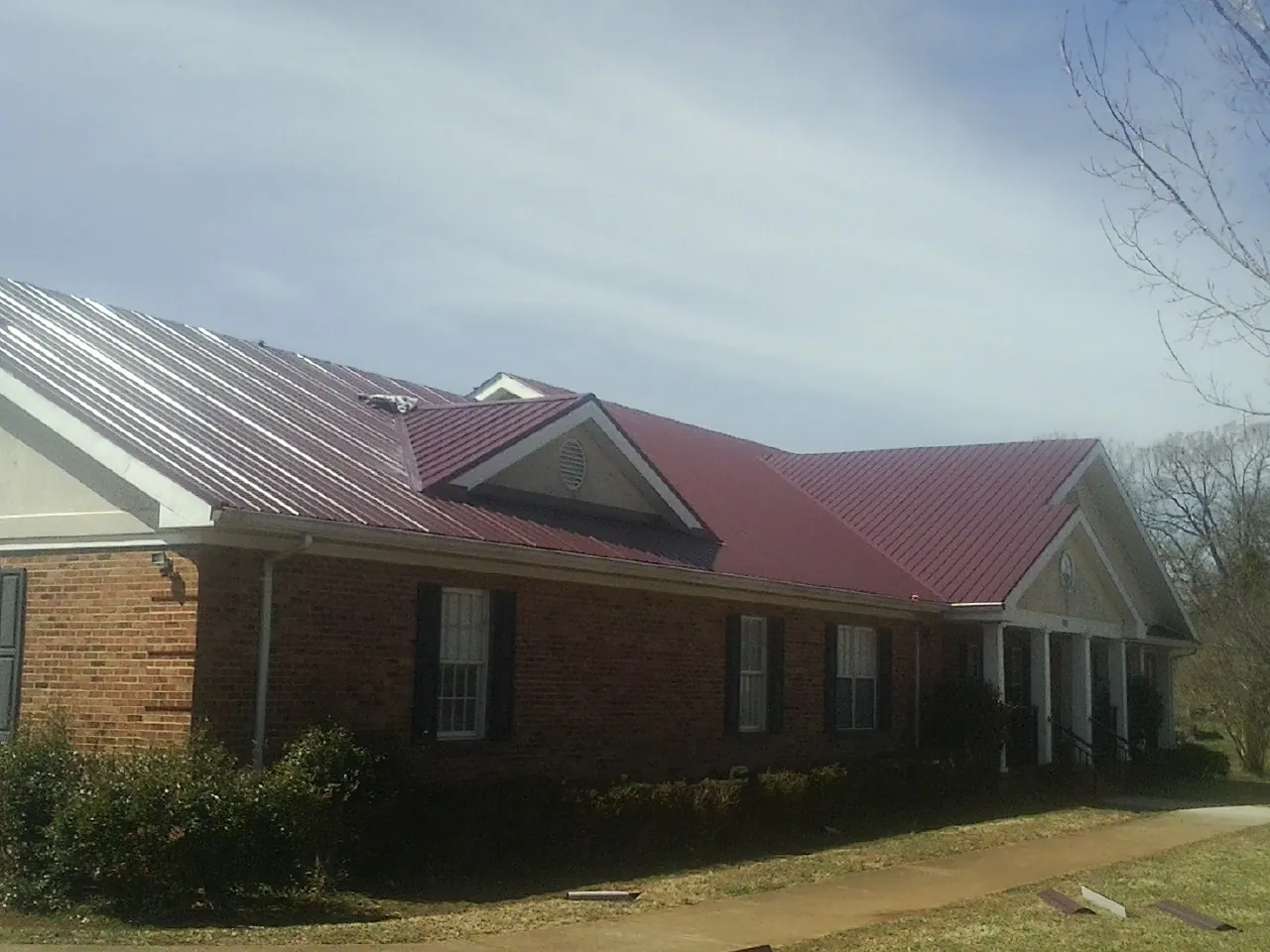Red metal roof with gabled entries on a long brick building, from a Hail Damage Roof Repair job in Chimayo