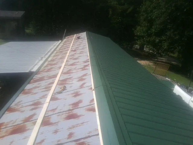 Old rusted panels beside newly installed green metal roofing — Wind Damage Roof Repair by Roofing Brothers in Chimayo