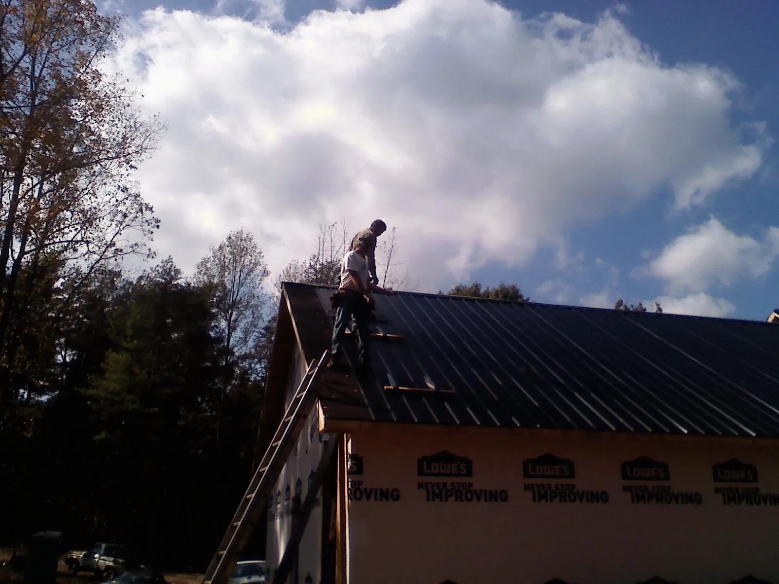 Roofer fastening dark metal panels high against a cloudy sky, from a Roof Inspection job in Chimayo