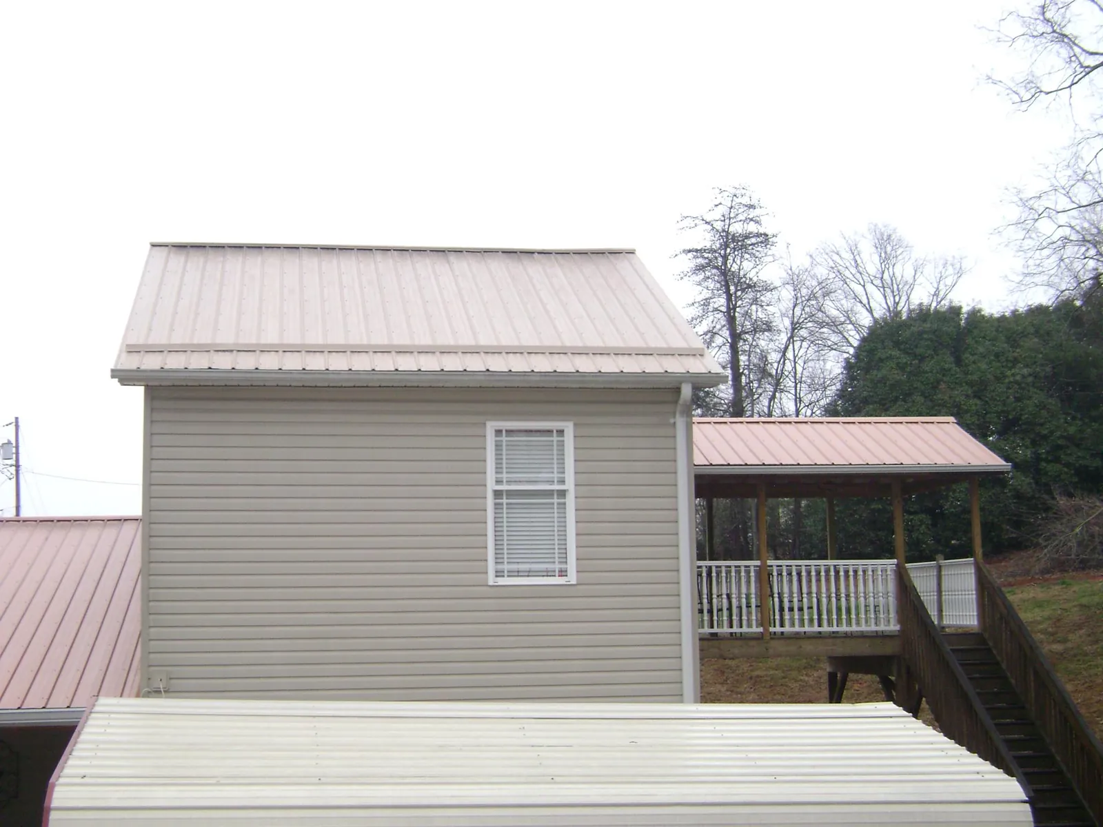 Tan metal roofs on a two story addition and attached porch in Chimayo